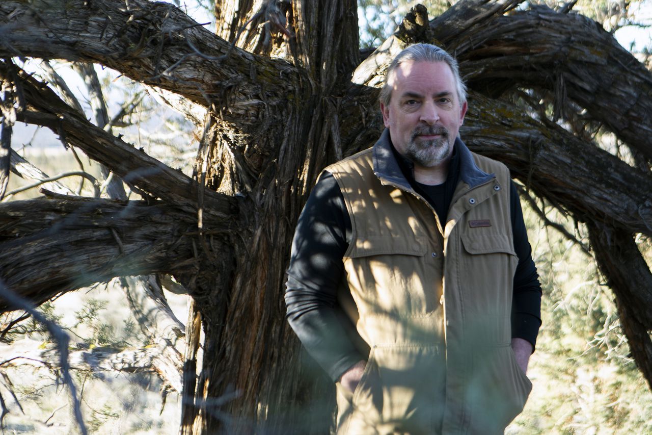 Stan Thomas stands outdoors in the shadow of a tree with his hands in his pockets.