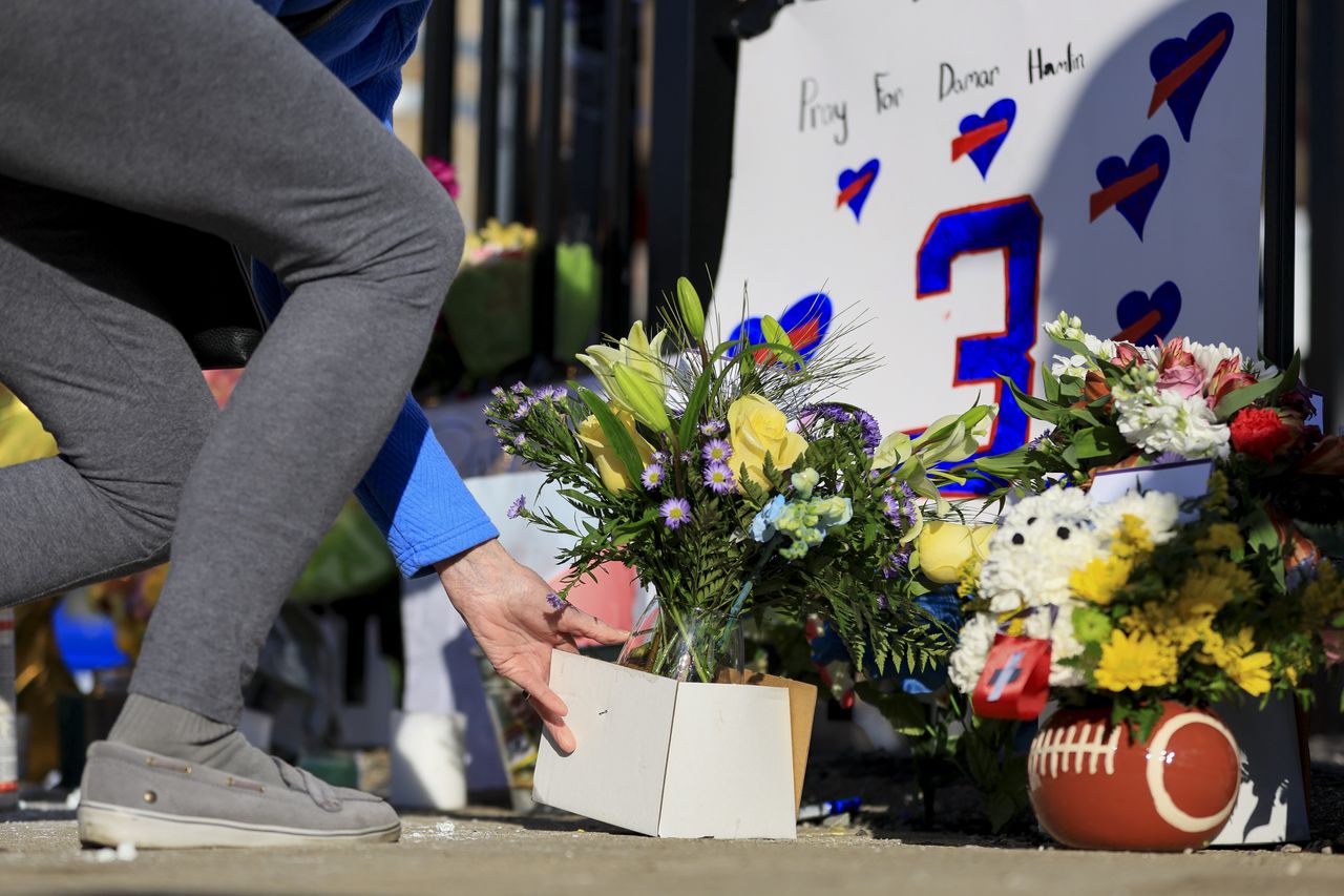 A person leans down to place a box of flowers near a tribute site for Hamlin.