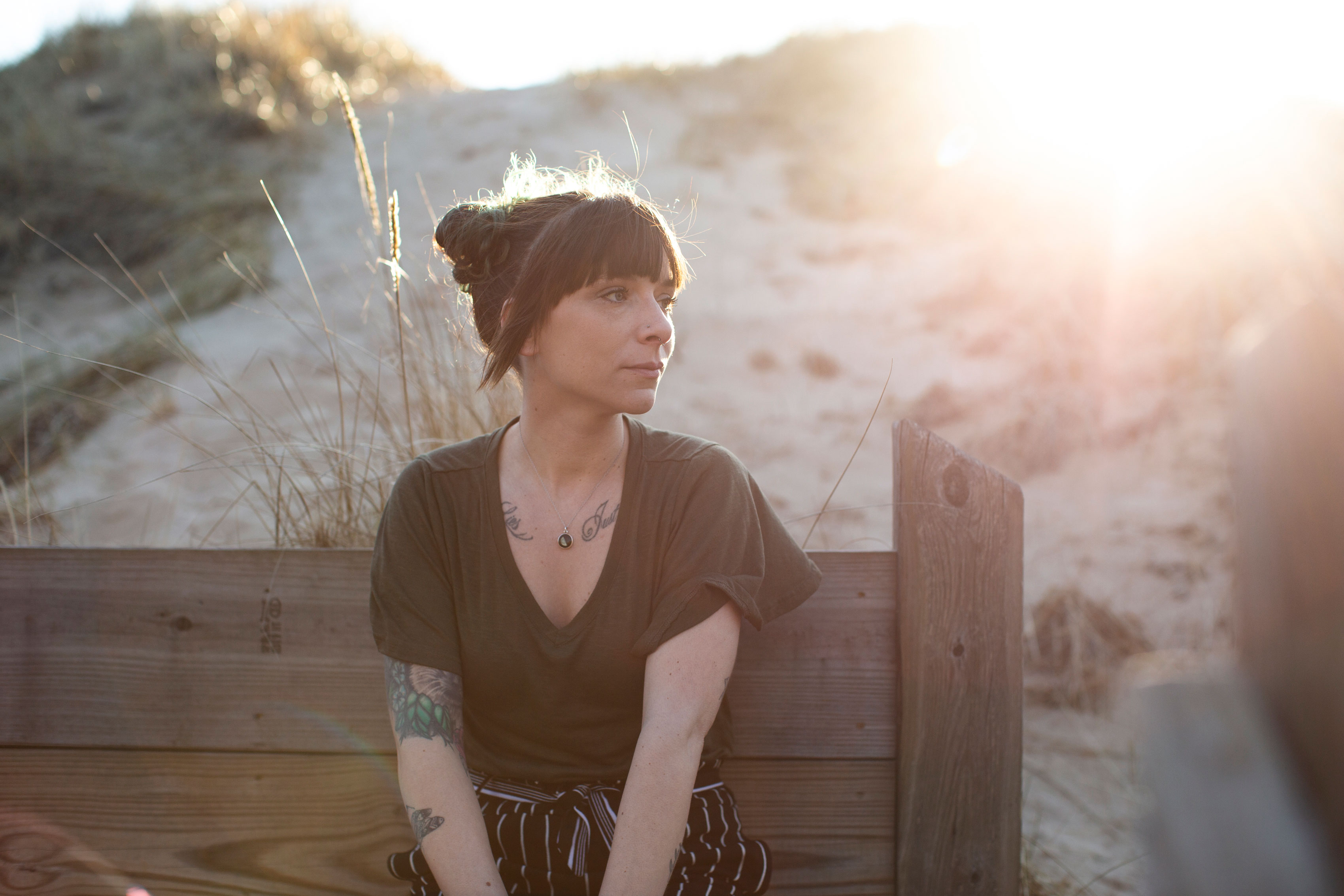 A woman sits on a wooden bench on a beach and looks off-camera to her left.